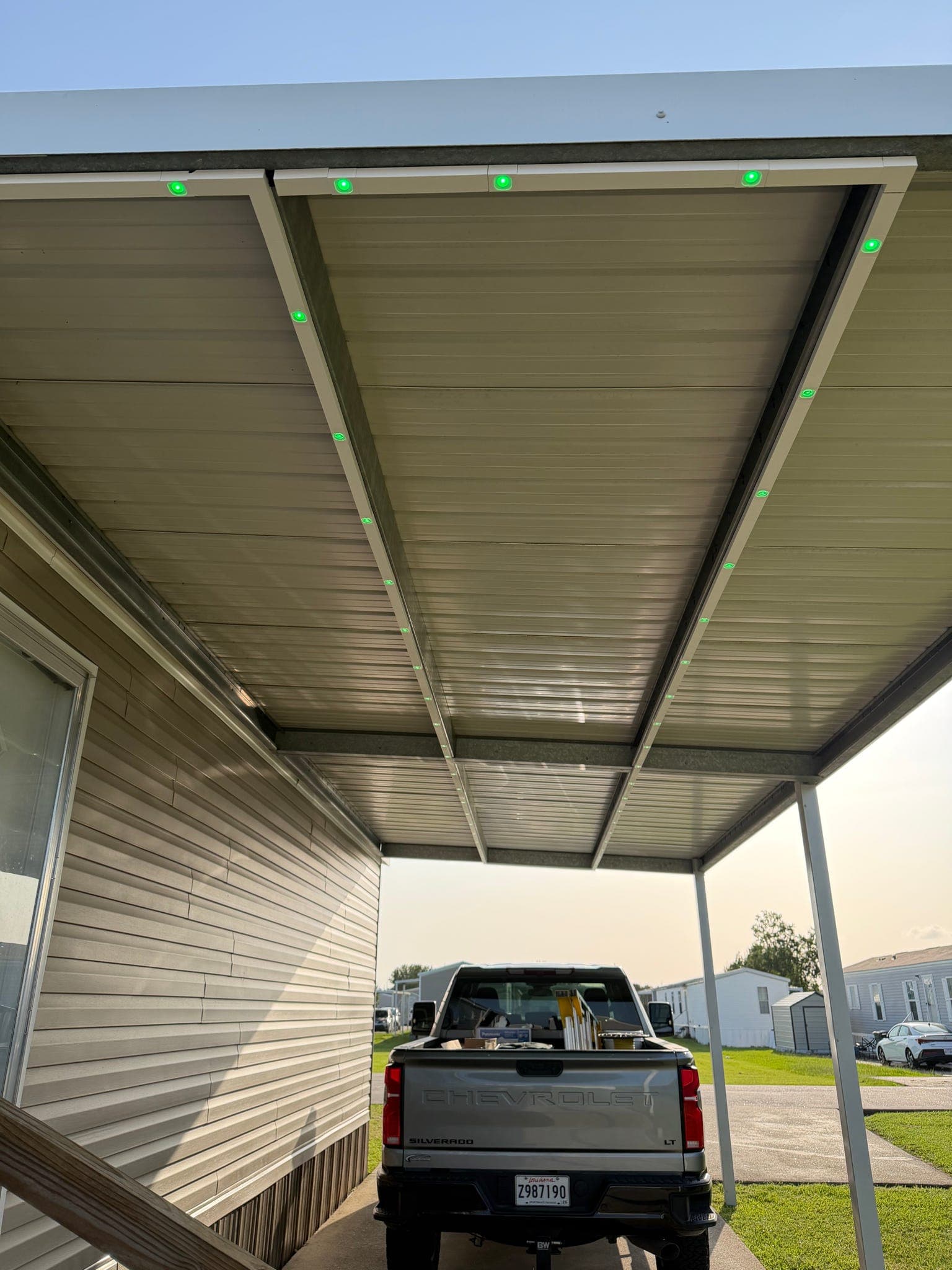 GeauxTrax matte white PETG channel installed under an aluminum carport soffit on a Louisiana mobile home — Govee Permanent Outdoor Pro pucks in green along the roofline