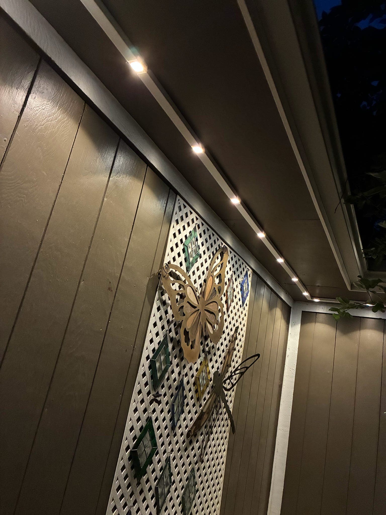 Close-up of GeauxTrax under a residential soffit at night — Govee Permanent Outdoor Pro pucks in warm white running the corner where two soffits meet, above painted wood siding