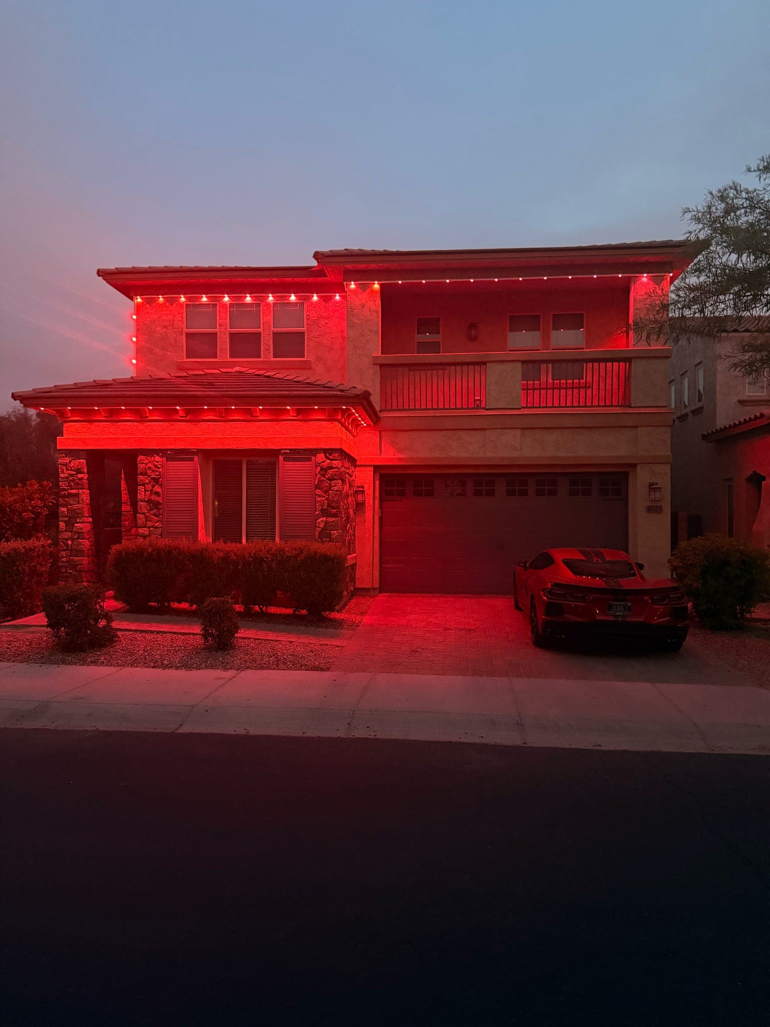 Two-story stucco home in Phoenix, AZ at dusk lit in solid red across the full roofline with GeauxTrax PETG track — Govee Permanent Outdoor Pro pucks visible along both the upper eave and the second-story balcony line