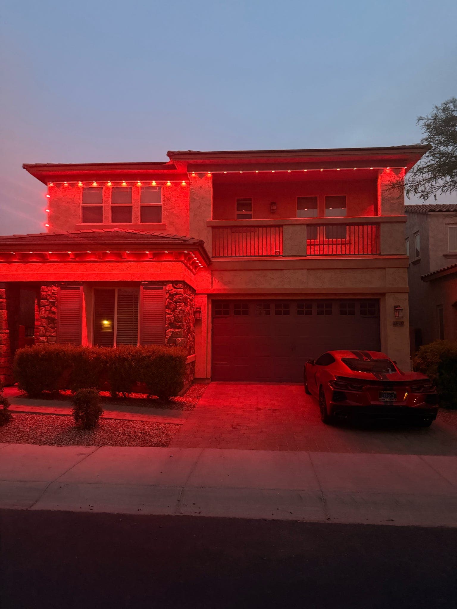 Same Phoenix, AZ two-story stucco home from a slightly different angle at dusk, Govee Permanent Outdoor Pro pucks in red across the roofline, wires hidden inside GeauxTrax PETG channel