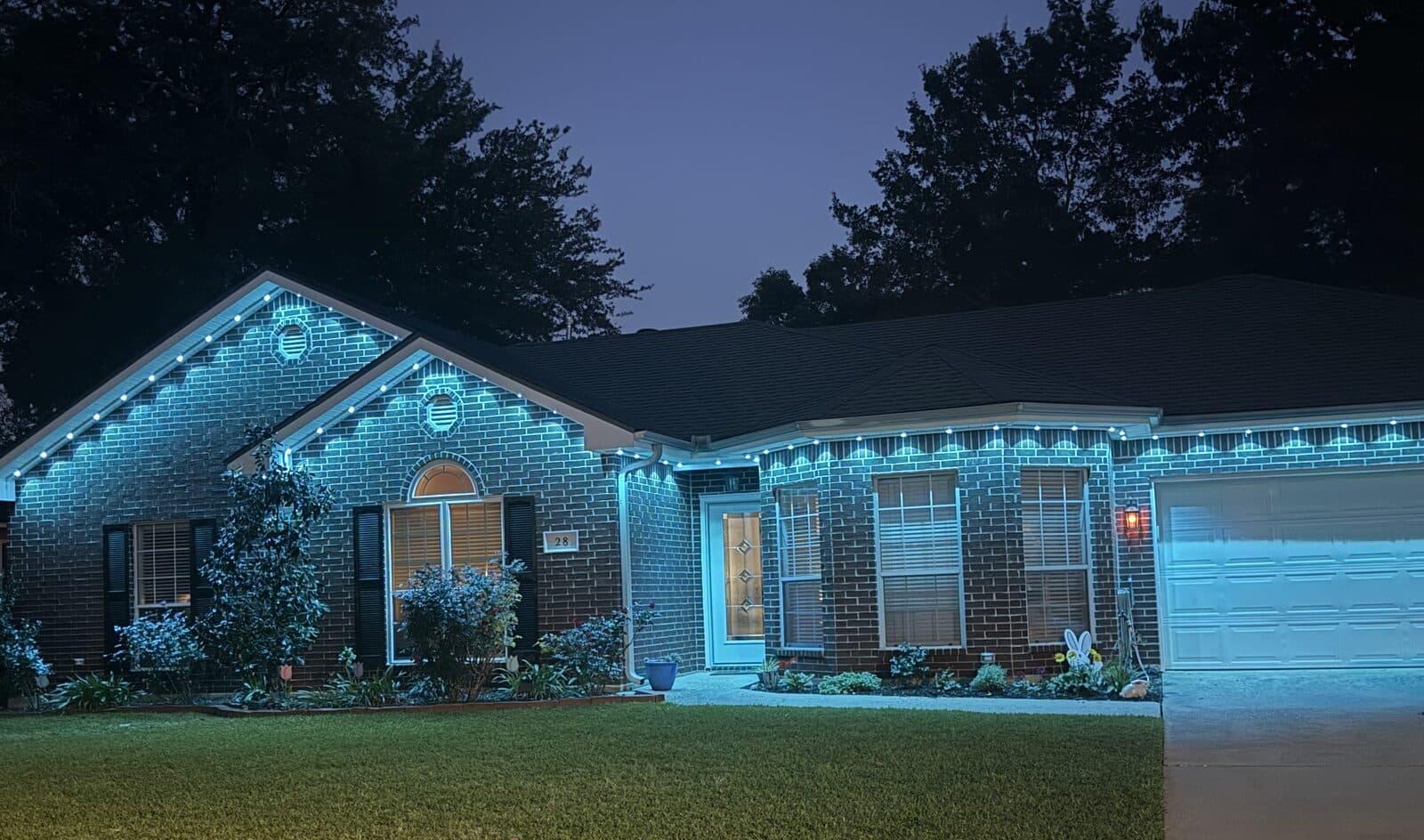 Single-story brick home at night with GeauxTrax-mounted Govee Permanent Outdoor Pro lights set to a solid teal color scene