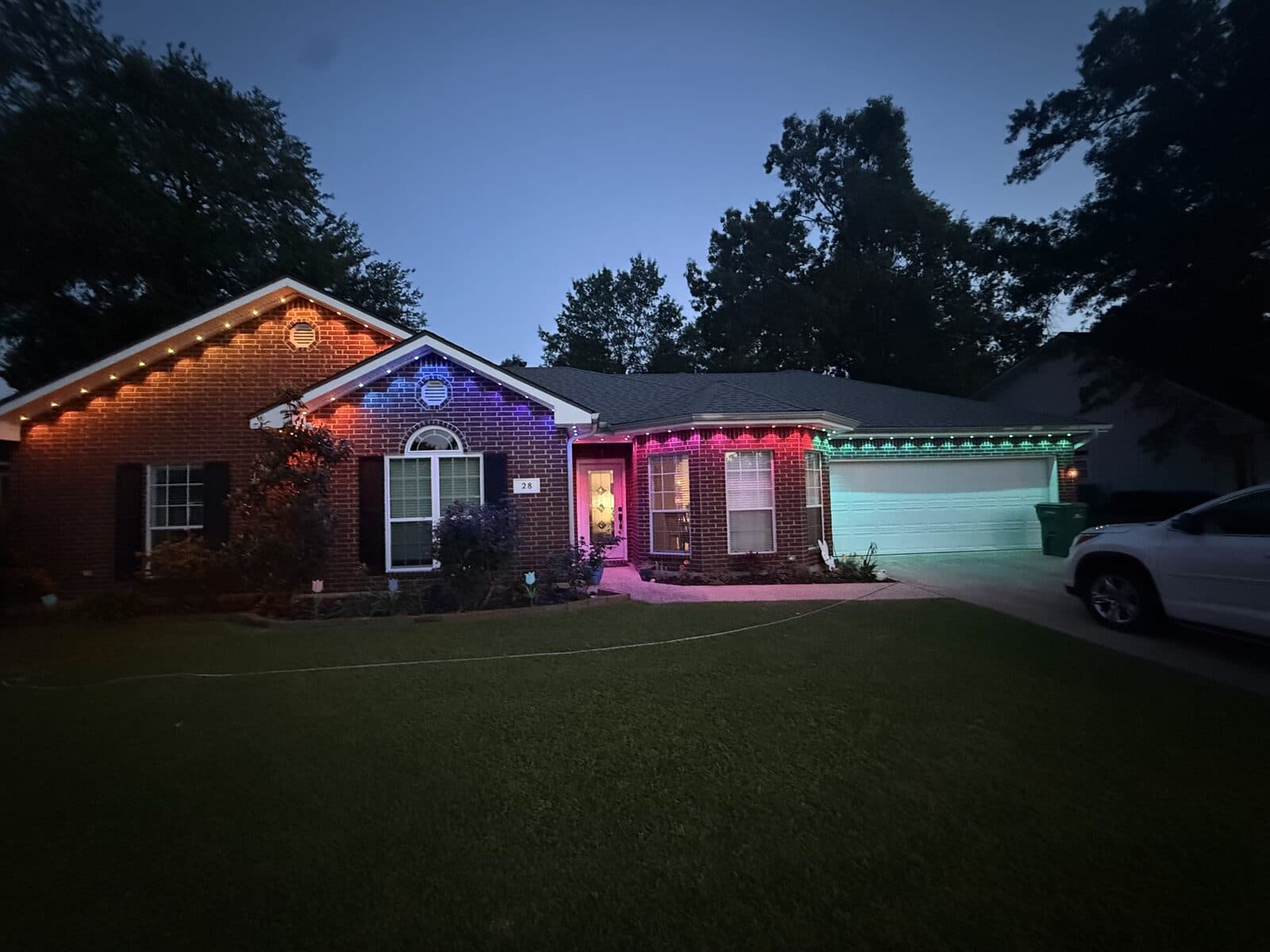 Single-story brick home with Govee Permanent Outdoor Pro in a multi-color scene — magenta over the front door, green over the garage — all wires hidden by GeauxTrax PETG track
